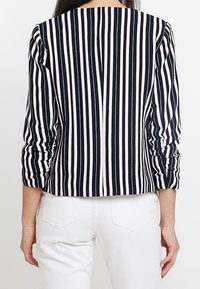 Veste blazer rayée marine et blanche avec manches longues froncées et encolure ronde, présentant un design court et une texture de tissu lisse.