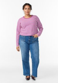 Prugasta majica dugih rukava u ružičastoj i bijeloj boji, uparena s plavim trapericama ravnog kroja. Tamne cipele upotpunjuju izgled.