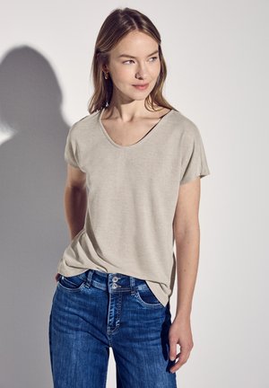 T-shirt beige a maniche corte con scollo ampio, texture morbida e vestibilità rilassata, abbinato a jeans blu in denim con chiusura a doppio bottone.