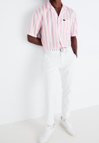 Kortärmad rosa och vit randig skjorta, vita byxor och vita sneakers med accenter. Ficka på skjortan; bälte med silverdetaljer.