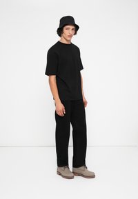 Camiseta de algodón negra, ajuste relajado, combinada con pantalones negros. Un sombrero de cubo negro y botas hasta el tobillo en gris claro con suelas marrones completan el look.