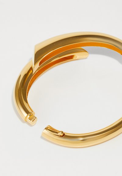 Goldfarbener Metallarmreif mit einem eleganten, geschwungenen Design und einer glatten, polierten Oberfläche sowie einer kleinen Öffnung für den Tragekomfort.