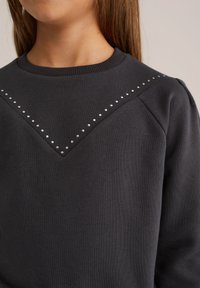 Felpa grigia scura con un design a zigzag e borchie argentate lungo il collo. Realizzata in cotone testurizzato con polsini a costine.