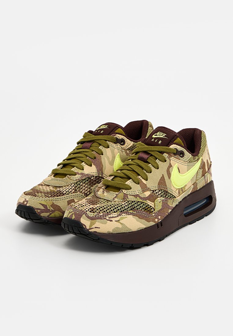 Zapatillas de deporte con patrón de camuflaje, parte superior de malla, detalles en cuero marrón oscuro y logo de Nike en amarillo brillante. Suela de goma negra.