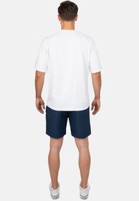 Witte katoenen t-shirt met korte mouwen, gecombineerd met marineblauwe shorts. De shorts hebben een soepele textuur en reiken boven de knie. Witte sneakers.