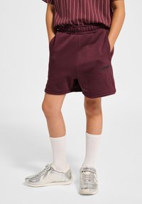 Bordeauxfärgade bomullsshorts med elastisk midja, sidofickor och en logodetalj. Matcher med vita knästrumpor och silverfärgade sneakers.