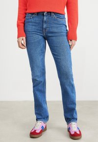 Modré džíny s rovnými nohavicemi, dokončené měděnými nýty a horním knoflíkem. Spárovány s vícebarevnými sportovními botami.