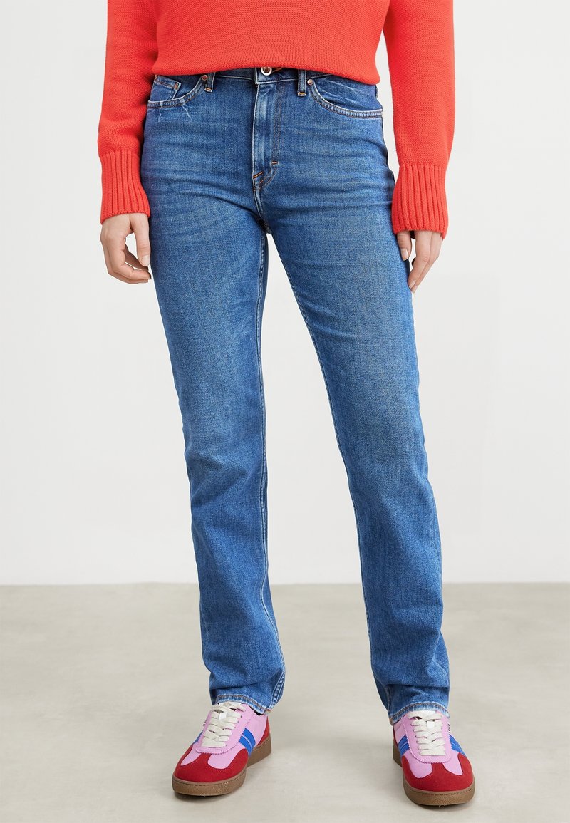 Modré džíny s rovnými nohavicemi, dokončené měděnými nýty a horním knoflíkem. Spárovány s vícebarevnými sportovními botami.