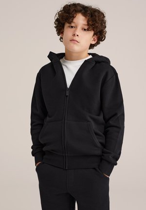 Zwarte rits hoodie gemaakt van zacht materiaal, met een voorrits, twee zijzakken en een capuchon. Gekleed met bijpassende zwarte broek.