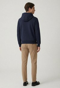 Felpa con cappuccio blu navy con finitura testurizzata, cappuccio con coulisse e orlo a costine, abbinata a pantaloni chino beige e scarpe nere.