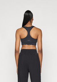 Μαύρος αθλητικός στηθόδεσμος με λοξές άκρες και σχέδιο ράστερ, συνδυασμένος με μαύρα φαρδιά παντελόνια. Λείο υλικό και ελαστική μέση.