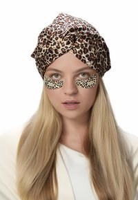 Turban mit Leopardenmuster, Augenpflaster mit ähnlichem Muster, blonde Haare, neutraler Oberteil, helle Haut. Klarer Hintergrund, Fokus auf Gesichtszüge.