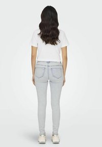 Uske slim-fit svijetloplave traperice s stražnjim džepovima, uparenim s običnom bijelom majicom. Model nosi bijele teniske, a kosa mu je stilizirana u labave valove.