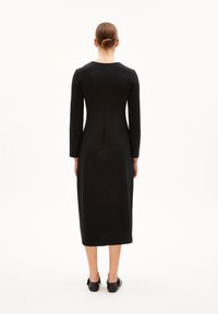 Schwarzes langärmliges Kleid mit taillierter Silhouette, knielang, Rundhalsausschnitt, glattem Stoff, minimalen Nähten und schlichtem Design.