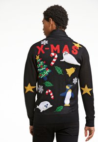Uomo con un maglione natalizio nero con il testo rosso "X-MAS", bastoncini di zucchero, albero di Natale, pinguino, foche, agrifoglio, campana, stelle e fiocchi di neve.