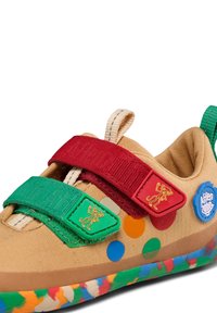 Chaussure beige pour enfant avec des scratchs verts et rouges, des pois colorés, logos de singe en dessin animé, et semelle en caoutchouc multicolore.