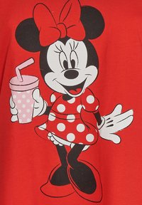 Camiseta roja con un personaje de dibujo animado con cara en blanco y negro, vestido con un vestido de lunares y sosteniendo una bebida rosa con una pajita.