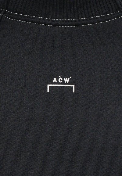 Melna adīta džemperis ar ribotu apkakli. Pamanāms balts grafisks logo "ACW*" centrā, vienkāršs un minimālistisks dizains.