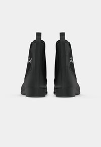 Botas de tornozelo pretas com uma textura suave, painéis laterais elásticos e um salto. Apresenta um logotipo bordado branco na parte de trás.