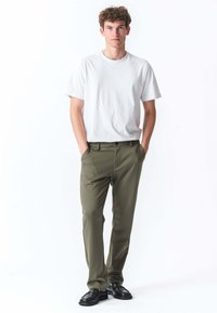 Hvid bomulds-T-shirt, olivengrøn skræddersyet bukser med forlommer og sorte sko. Glat tekstur, tætsiddende design, minimalistisk stil.