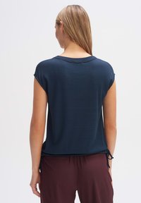 Top blu navy a maniche corte con effetto a righe, scollo rotondo e lacci ai lati, abbinato a pantaloni bordeaux. Tessuto morbido.