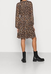 Vestido negro con volantes y un patrón irregular en naranja y blanco, de manga larga y con un cinturón, acompañado de botas negras gruesas hasta el tobillo.