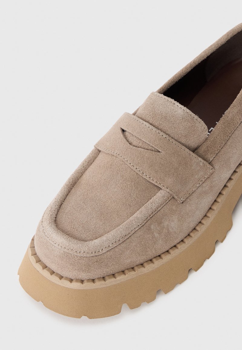 Beige Wildleder Slipper mit einem rechteckigen Oberriemen, einer runden Zehenpartie und einer dicken Gummisohle mit tiefen Rillen für besseren Halt.