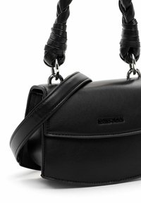Bolso de piel negra con forma curvada, asa trenzada en la parte superior y correa ajustable. Presenta un solapa frontal con un logo sutil.