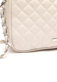 Borsa a tracolla sintetica color beige chiaro imbottita con tracolla a catena, caratterizzata da una texture liscia e dettagli di cucitura sottili.