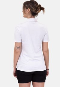 Polo shirt bianco a maniche corte con colletto classico, texture morbida e dettaglio a fondo spacco. Abbinato a pantaloni corti neri.