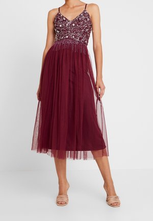 Ärmelloses bordeauxfarbenes Midikleid mit paillettenverziertem Oberteil, transparentem Überrock und dünnen Trägern, getragen mit nudefarbenen offenen Sandaletten mit Absatz.