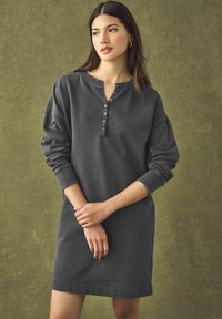 Robe-sweat gris foncé avec un col henley, sept boutons sur le devant, épaules tombantes et poignets côtelés. Texture lisse.