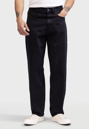 Schwarze Jeans aus Denim mit geradem Bein, fünf Taschen und einem Knopfverschluss. Getragen mit weißen Canvas-Sneakern.
