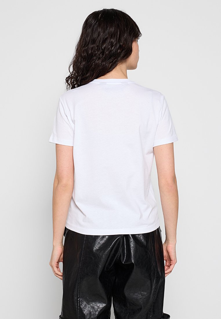 Camiseta blanca de manga corta con cuello redondo. La tela parece suave. Se combina con pantalones negros sueltos y brillantes. Diseño simple y limpio.