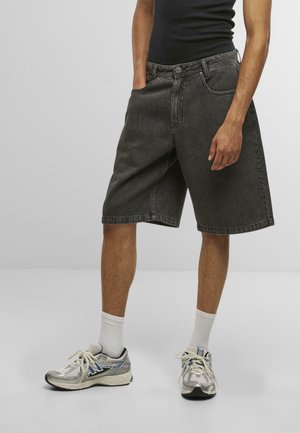 Sorte denimshorts med en afslappet pasform, udstyret med et femlomme-design og synlige sømme. Båret med grå sportssko og hvide sokker.
