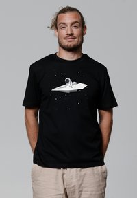 Schwarzes Baumwoll-T-Shirt mit einem Grafikdruck eines Astronauten auf einem Papierflugzeug vor einem dunklen, weltraumthematischen Hintergrund mit weißen Sternen.
