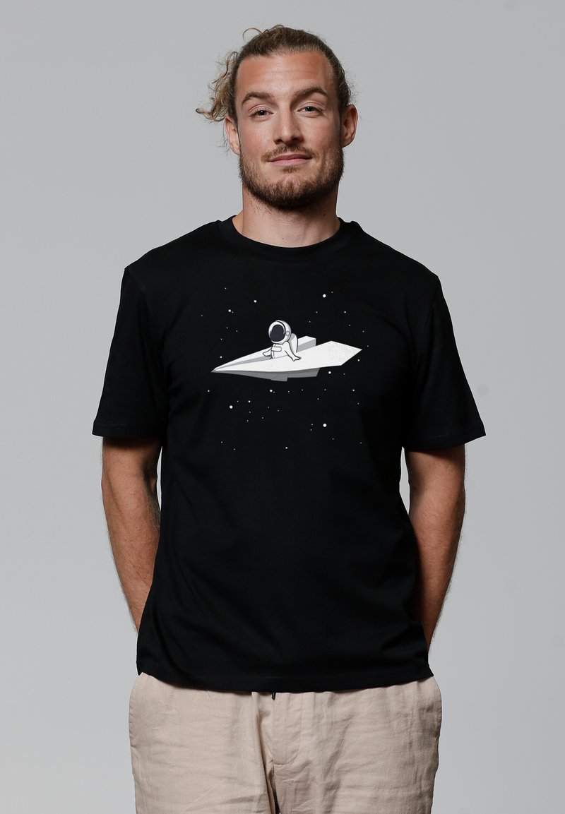 Schwarzes Baumwoll-T-Shirt mit einem Grafikdruck eines Astronauten auf einem Papierflugzeug vor einem dunklen, weltraumthematischen Hintergrund mit weißen Sternen.