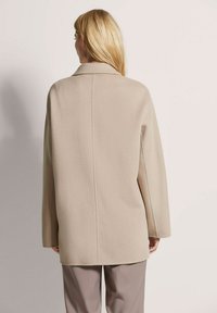 Beige wollen blend jas met een ontspannen pasvorm, enkele kraag en lange mouwen. Heeft een eenvoudige achterkantnaad en valt onder de heup.