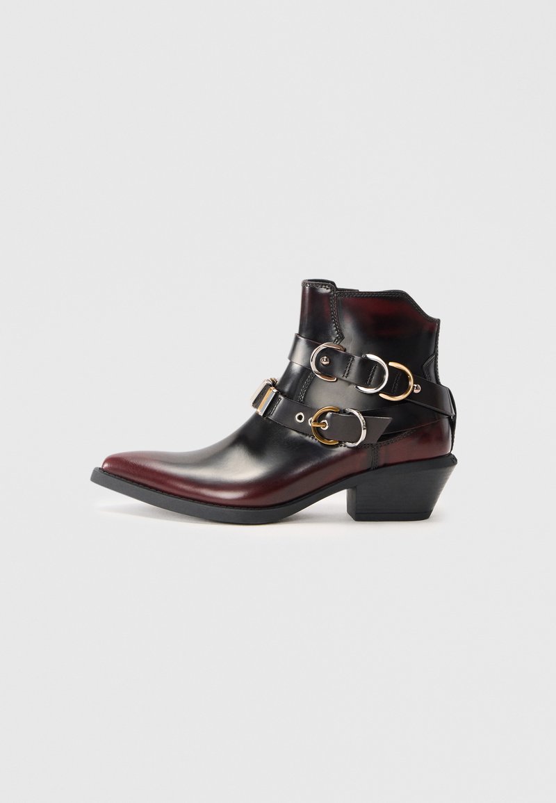 Bottine en cuir noir et rouge foncé avec un bout pointu, un talon carré et trois sangles décoratives à boucle autour de la cheville.