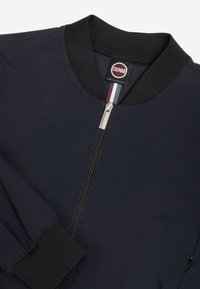 Temno modra bomber jakna z rebrastim ovratnikom in manšetami, sprednjo zadrgo ter oznako Colmar Originals na notranji strani ovratnika z detajlom tkanine v črtah.