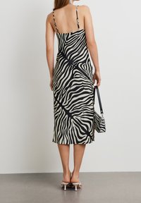 Mustavalkoinen sapelikuosisessa midi-mekossa on ohutolkaimet, tiukka siluetti ja sivuavomus. Mekko on yhdistetty samanlaiseen laukkuun.