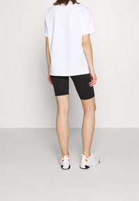 Witte katoenen t-shirt, zwarte fietsbroek en witte schoenen met oranje accenten. Focus op eenvoudig ontwerp en getailleerde vorm.