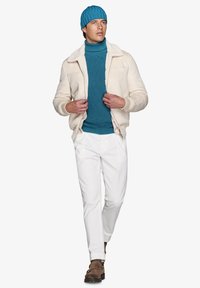 Beige shearling jakke, teal strikket sweater og matchende hat, hvide bukser og brune støvler, båret af en person der går.
