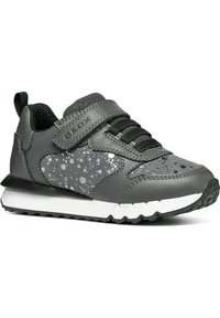 Zapatilla sintética gris con malla negra texturizada, correa de Velcro y acentos plateados punteados. Media suela blanca y suela negra con patrón de surcos.