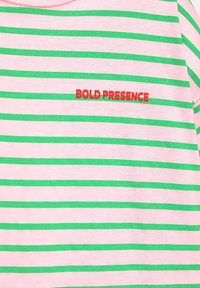 Chemise rose avec des rayures horizontales vertes et un texte rouge "BOLD PRESENCE" sur la poitrine.