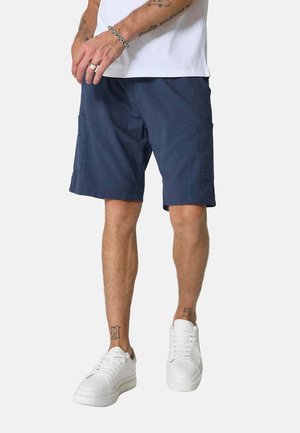 Shorts de cargaison navy avec poches latérales, fabriqués en tissu léger. Portés avec des baskets blanches. Présentent une coupe droite et un design décontracté.