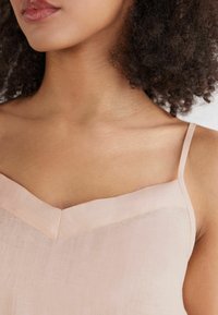 Camiseta sin mangas de color rosa claro con escote en V, tirantes finos y una tela texturizada. Presenta un diseño limpio y minimalista con detalles de costura sutiles.