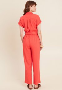 Combinaison coral avec des manches courtes, une taille ceinturée et des pantalons à jambes droites. Fabriquée en tissu léger avec une texture subtile.