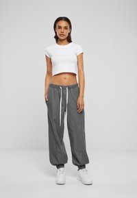 Gray, loose-fit pants with elastic cuffs and waistband featuring a white drawstring. Paired with a short-sleeve white cropped top and white sneakers.