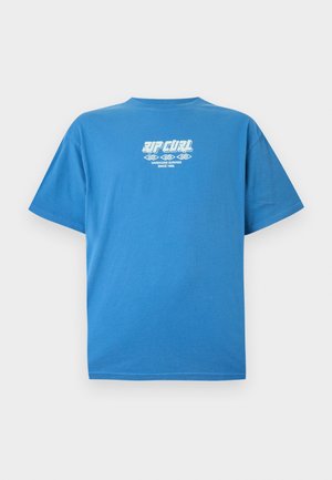 Blå T-shirt med korte ærmer med hvid tekst "RIP CURL Hardcore Surfing Since 1969" og dekorativt bølgemotiv midt foran.